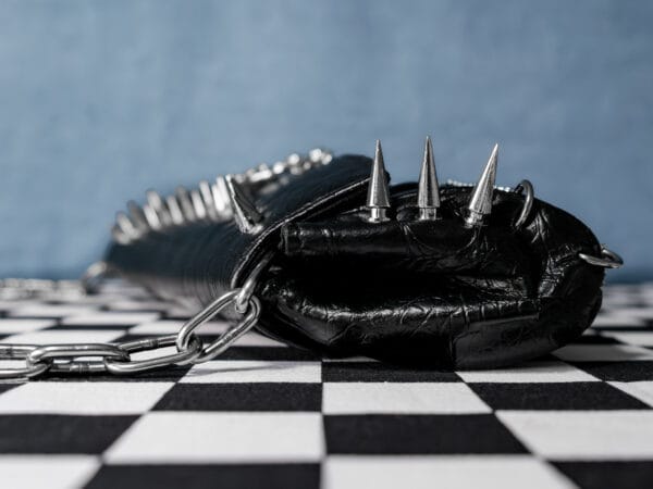 a product photo of a black faux leather handbag with spikes and chains.