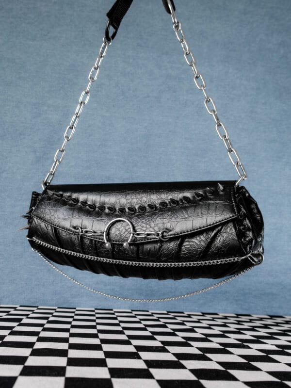 a product photo of a black faux leather handbag with spikes and chains.