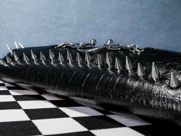 a product photo of a black faux leather handbag with spikes and chains.