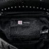 a product photo of a black faux leather handbag with spikes and chains.