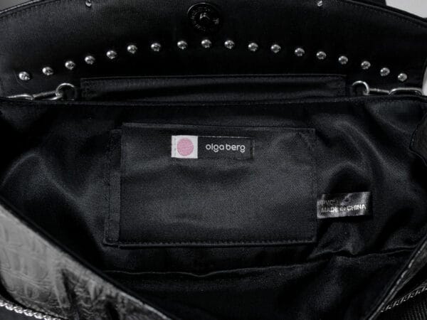 a product photo of a black faux leather handbag with spikes and chains.