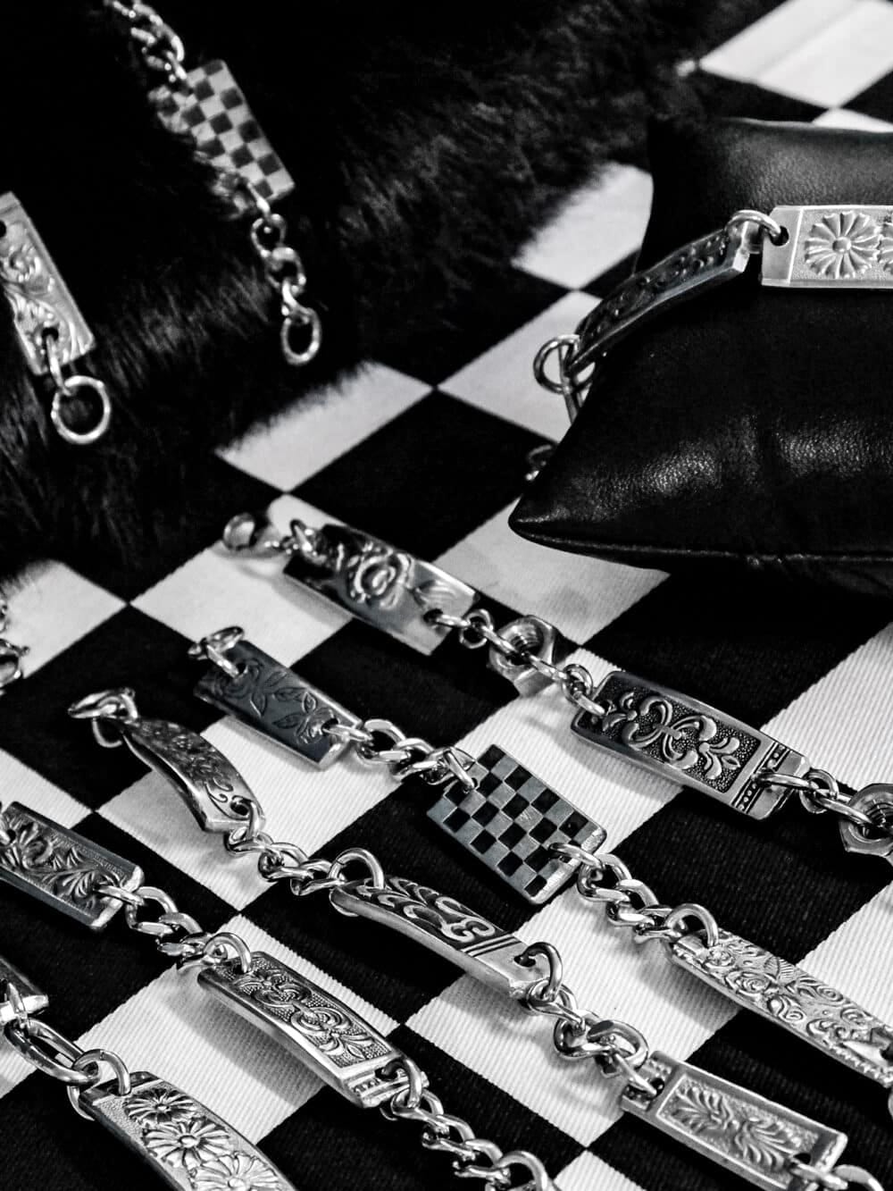 Decorative silver bracelet segments with floral engravings laid out on a black-and-white checkerboard fabric.