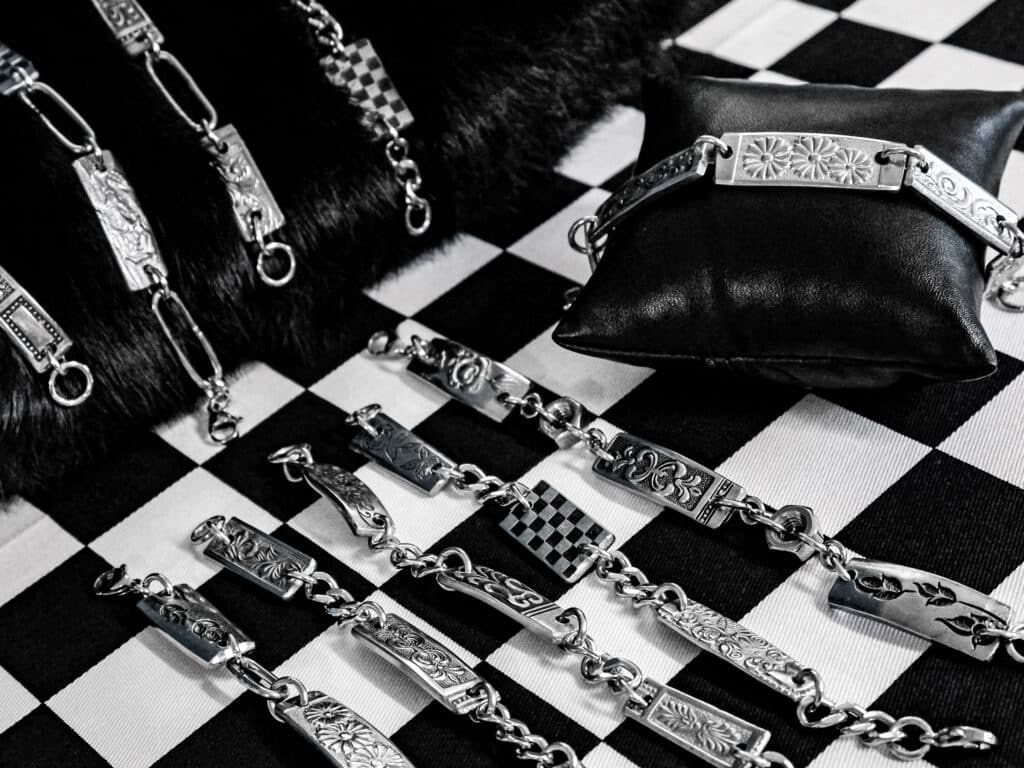 Decorative silver bracelet segments with floral engravings laid out on a black-and-white checkerboard fabric.